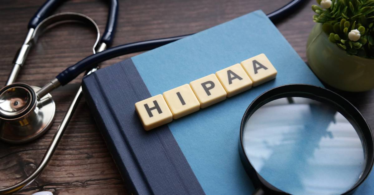 A blue book with tiles that spell out "HIPAA" resting on the cover. A magnifying glass and stethoscope surround it.
