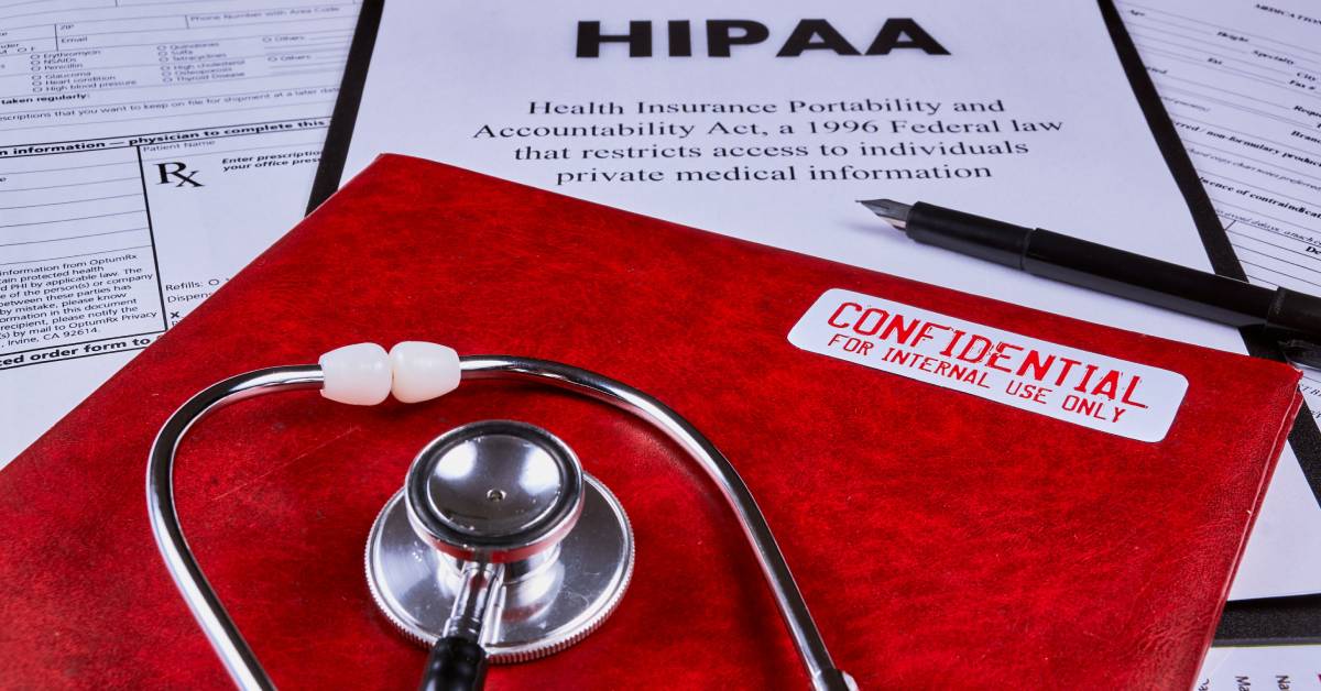 A red filing folder with a CONFIDENTIAL sticker on the cover and a stethoscope on top of it rests on top of HIPAA paperwork.