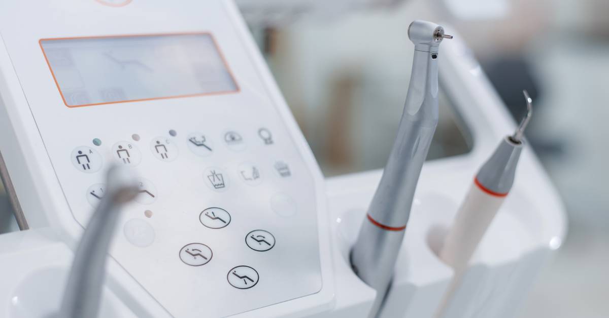 A close-up of a dental machine stand and monitor with three connected handheld pieces of dental equipment.